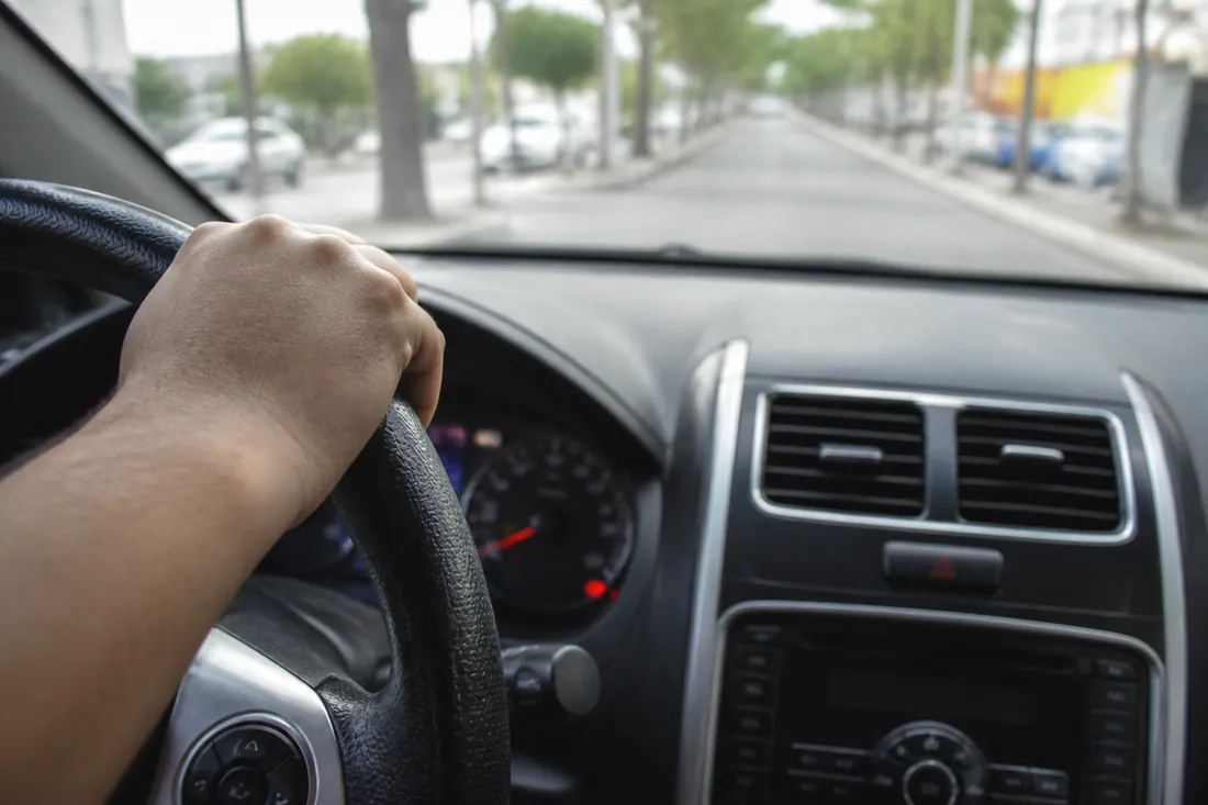 Motorista com a mão no volante e o painel do carro em foco